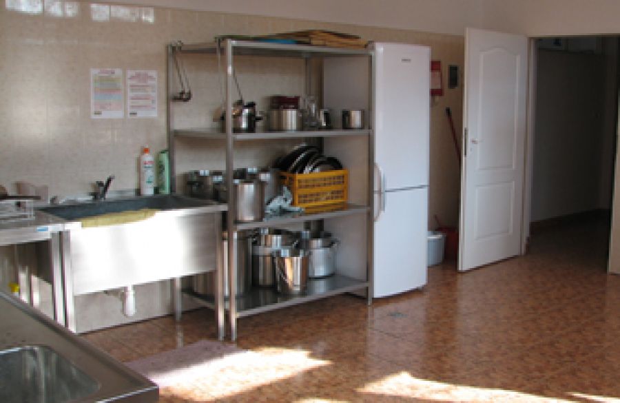 Wnętrze kuchni ze zlewem, półką z naczyniami i lodówką.