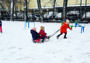 Dziewczynka ciągnie sanki, na których siedzą jej koleżanki.