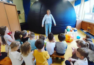 Dzieci siedzą na ławkach przed wejściem do planetarium.