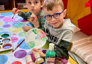 Dwóch chłopców maluje farbami papierowe talerzyki.