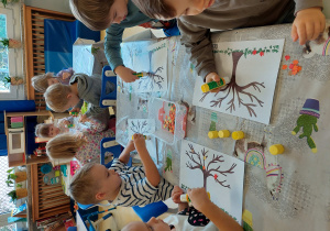 Dzieci wyklejają szablon drzewka.