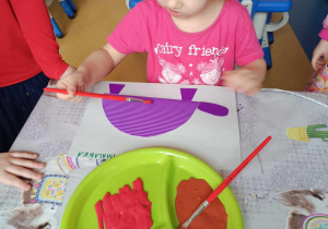 Dziewczynka maluje farbami dinozaura.