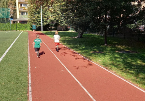 Tydzień olimpijski. Dzieci ścigają się w parach na bieżni na boisku szkolnym.