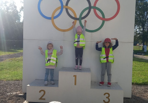 Wycieczka do Centrum Olimpijskiego. Troje dzieci stoi na podium olimpijskim.