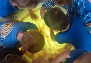 Dzieci manipulują ryżem leżącym na stoliku sensorycznym.