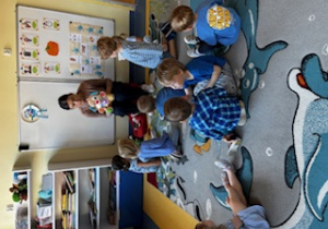 Dzieci siedzą na dywanie i słuchają pani od angielskiego.