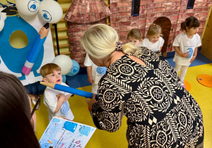 Pani Dyrektor ma duży ołówek w ręku i pasuje najmłodsze dzieci na przedszkolaka.