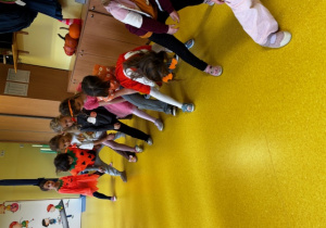 Dzieci są ustawione jedno za drugim i podają sobie dynie pomiędzy nogami.