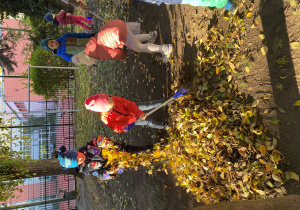 Dzieci sprzątają ogródek grabiąc liście.