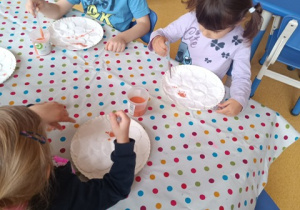 Dzieci siedzą przy stoliku i koloroują pipetą szablon dyni.