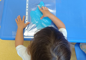 Dziewczynka rozprowadza farbę za pomocą pacy u rąk.