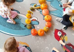 Dzieci siedzą na dywanie i układają kształty z dyń.