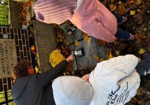 Nauczycielka i dzieci zapalają znicz w miejscu pamięci narodowej.