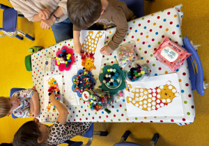 Dzieci wyklejają misia pomponami.