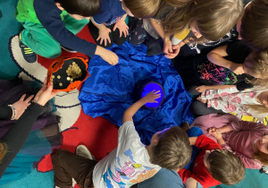 Wróżby Andrzejkowe, dzieci wrzucają monetę do kociołka.