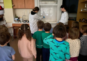 Eksperymenty w szkole, dzieci obserwują doświadczenie za szybą.