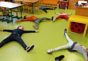 Dzieci leżą na podłodze z szeroko rozłożonymi rękami i nogami.