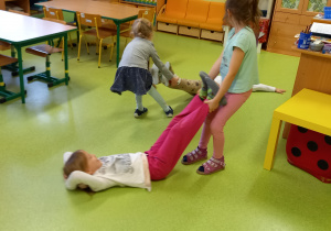 Dzieci ćwiczą w parach. Jedno dziecko przesuwa drugim po podłodze trzymając rówieśnika za nogi.